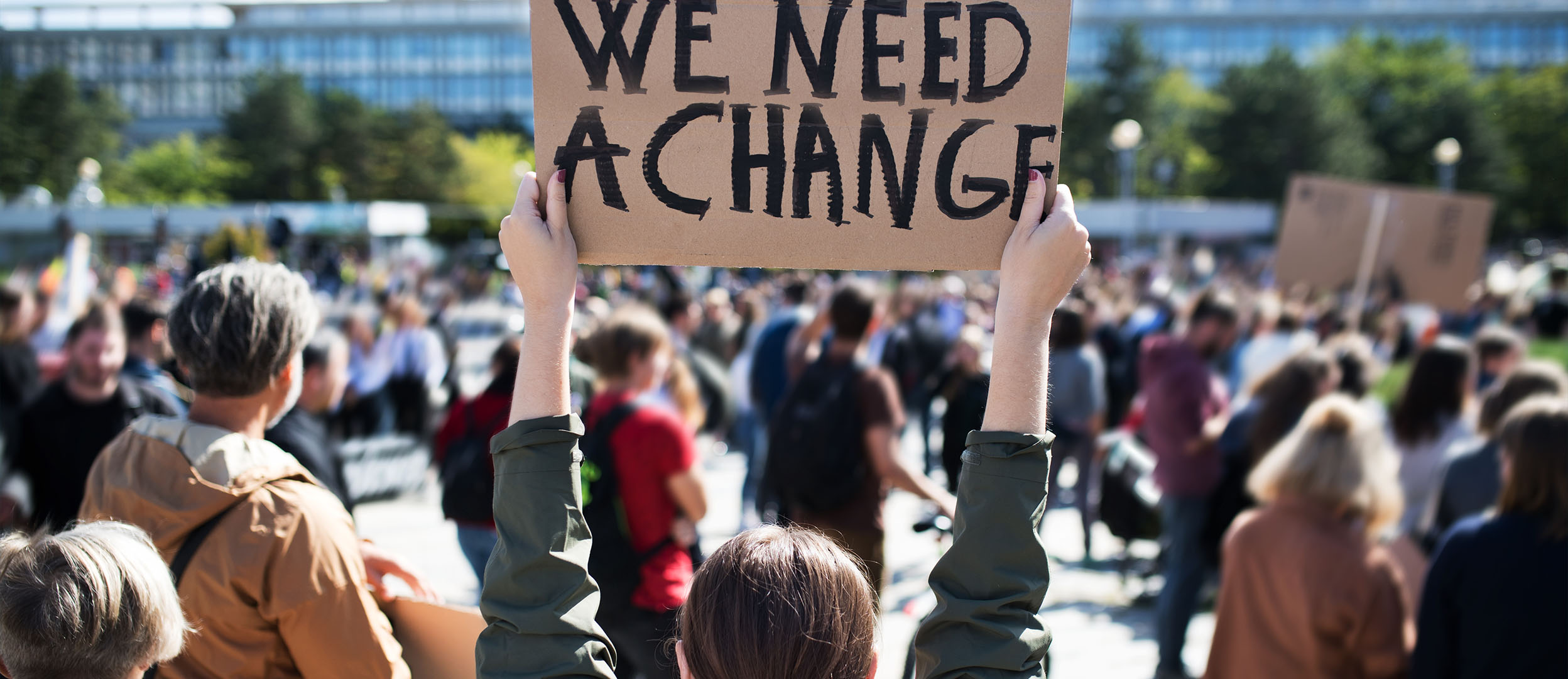 Woman at protest holds sign that reads “We Need Change”